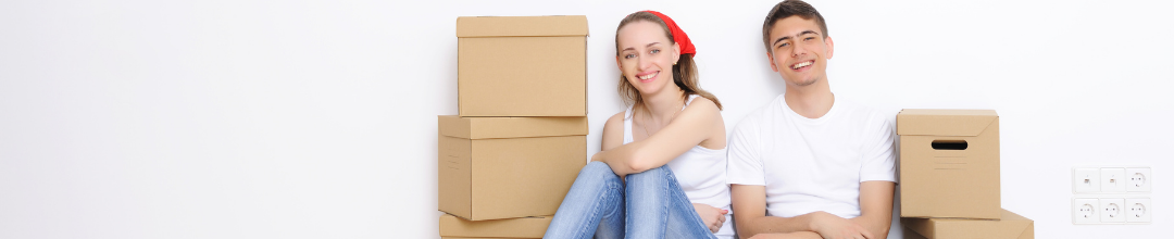 A young man and woman sitting against the wall with moving boxes