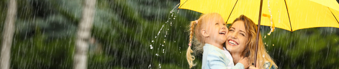 A woman and her young daughter smiling under a yellow umbrella while it rains