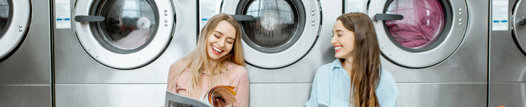 Two women sitting in front of a row of washing machines