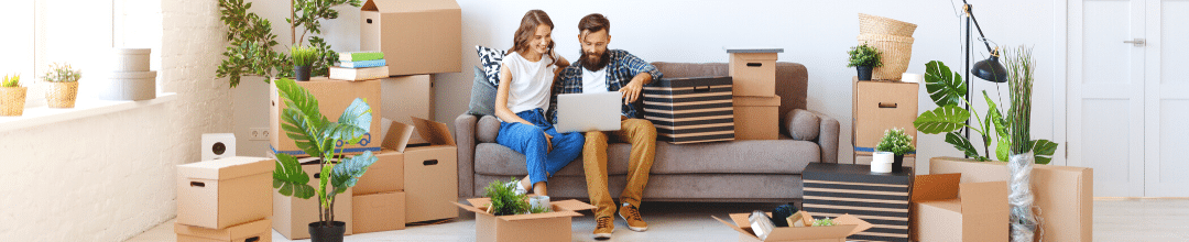 A young couple looking at a laptop in their new living room surrounded by moving boxes